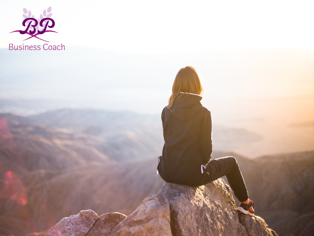 a lady sits on a rock at the top of a mountain, showing you can achieve amazing things if you get rid of limiting beliefs